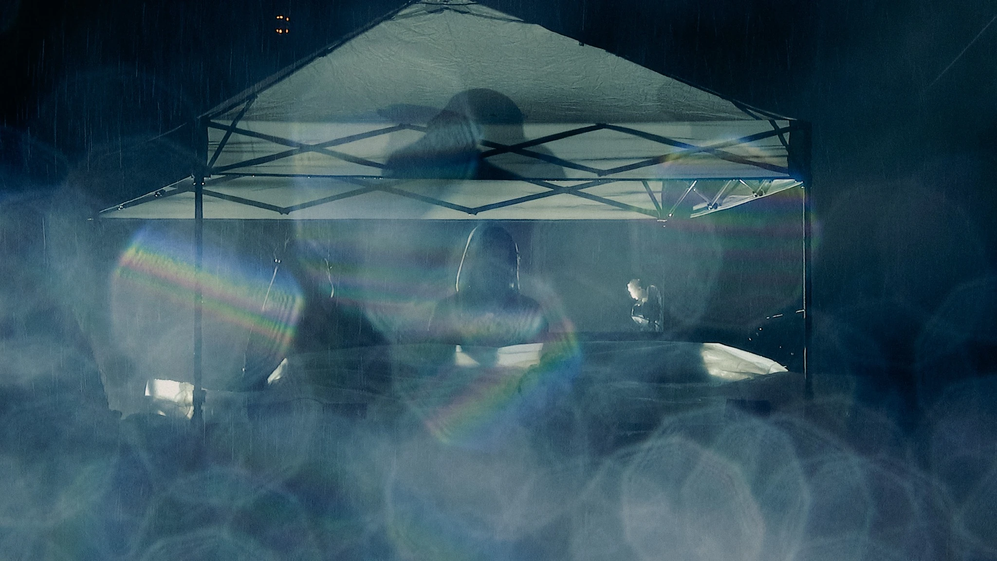 A silhouetted performer under a rain-soaked canopy