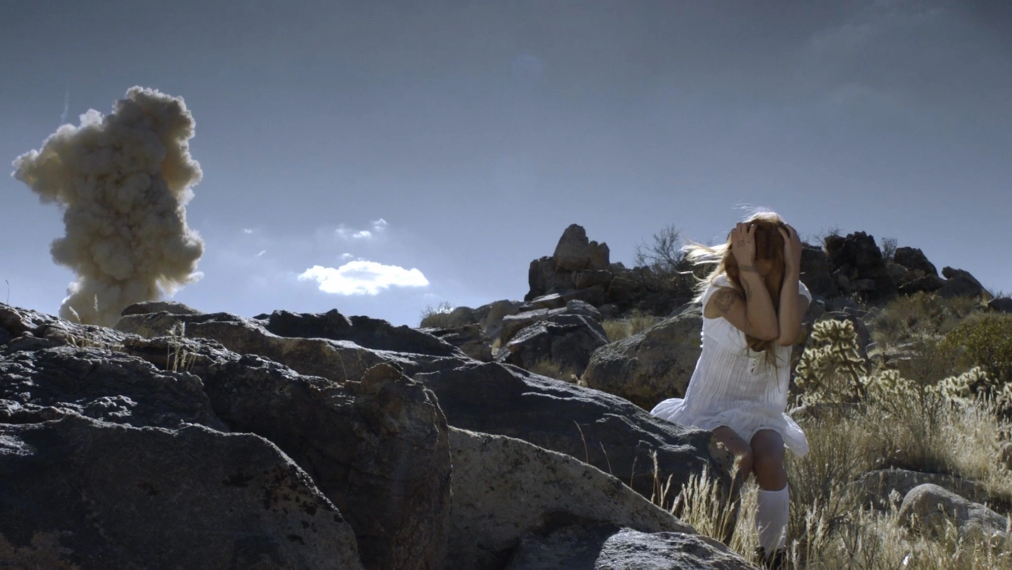 Tiffany Day seated among desert rocks beside a rising plume of smoke