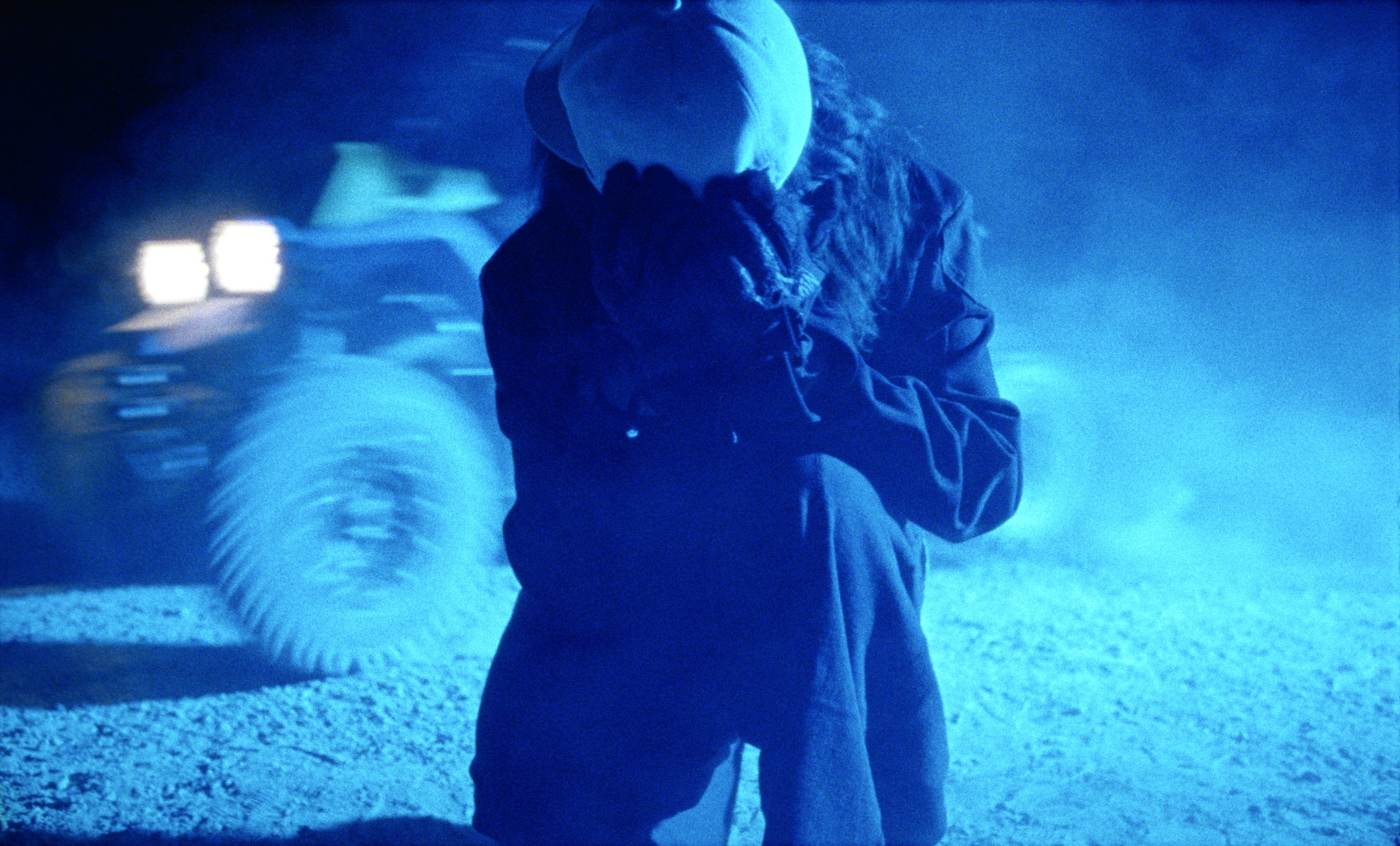 A figure in blue light with a vehicle behind them
